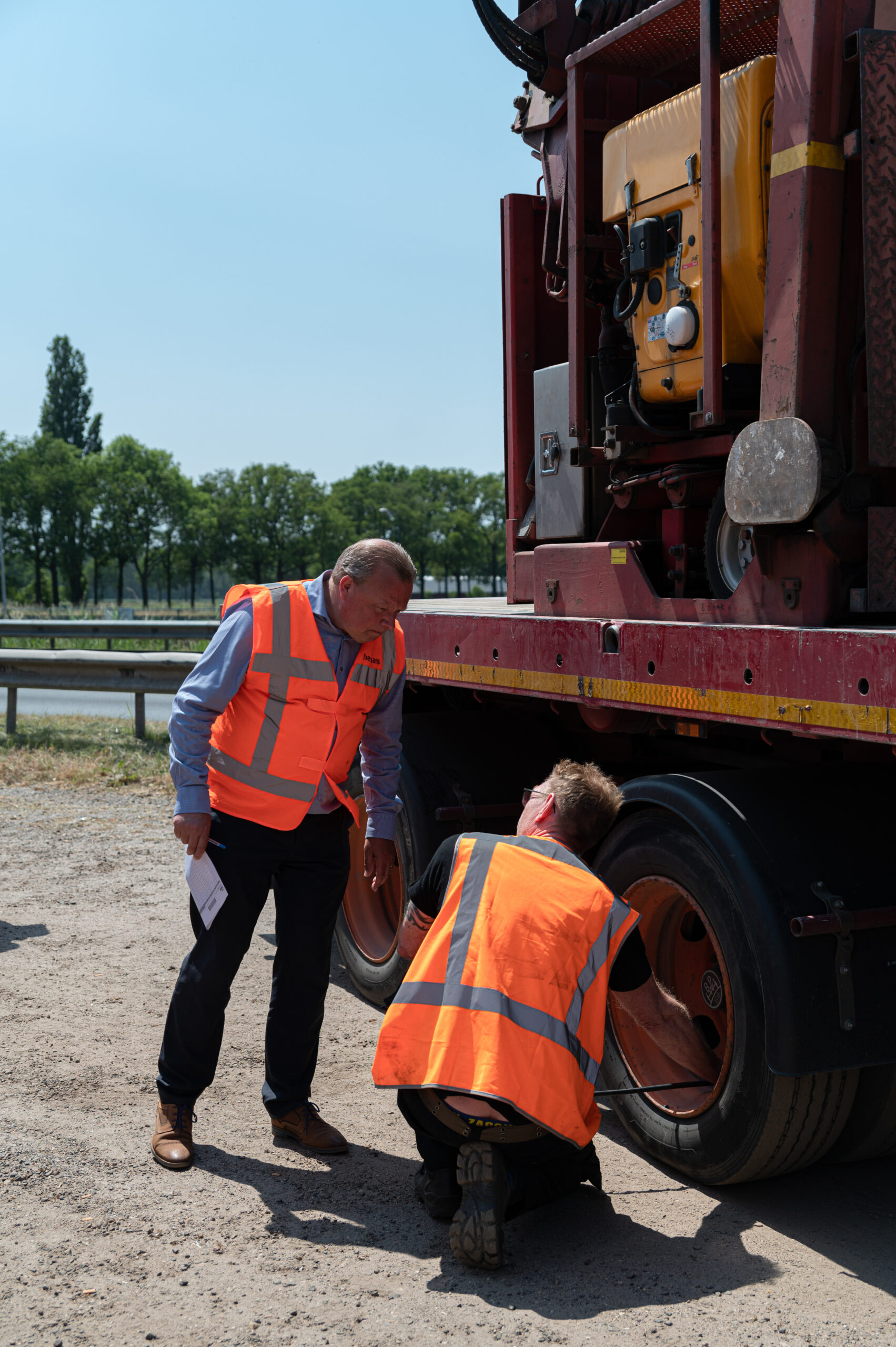 Photo of two gentlemen wearing orange safety vests standing next to a large truck doing a tire check