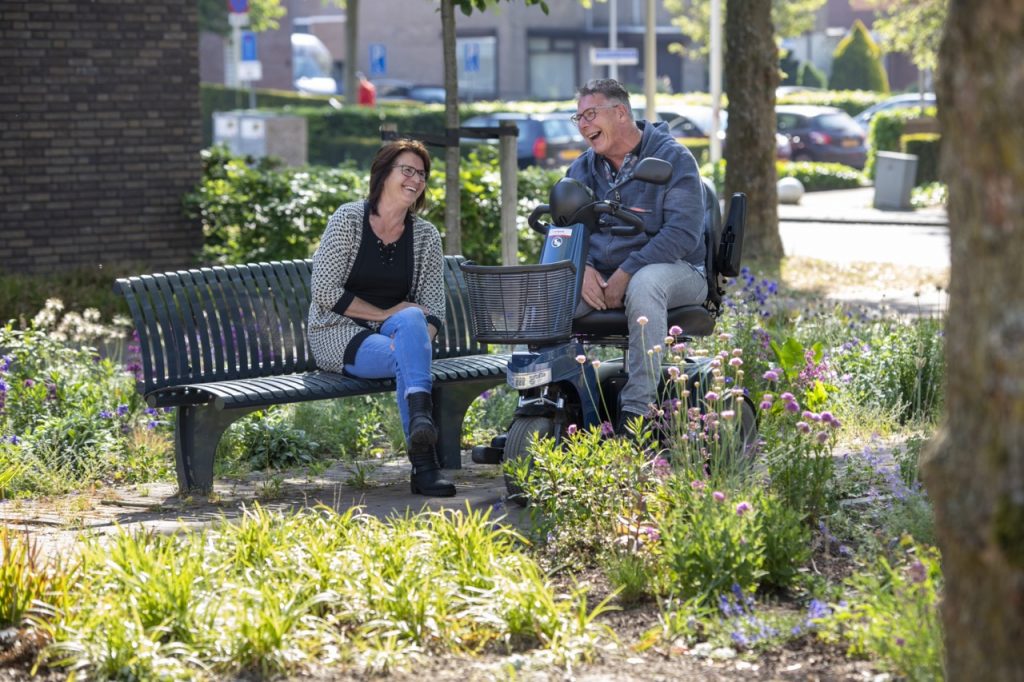 Foto van man (op scootmobiel) en vrouw op een stadspark bankje