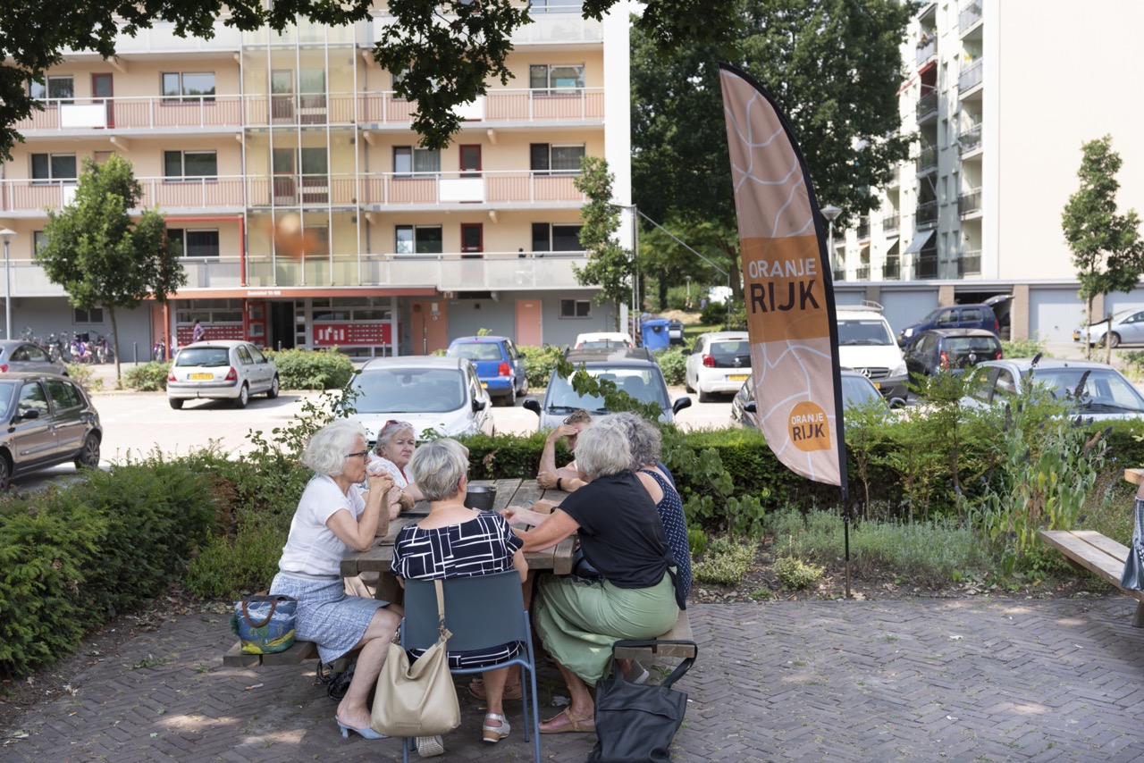 Foto van een groepje senioren op een picknicbankje in een stadsbuurt