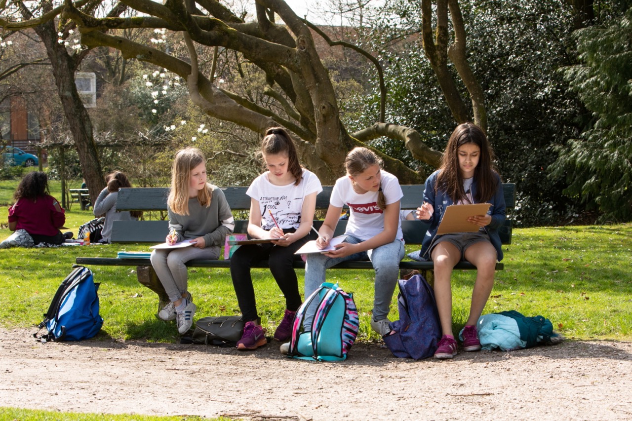 Foto van vier scholieren op een bankje in het park in lekker weer tijdens de landelijke buitenlesdag