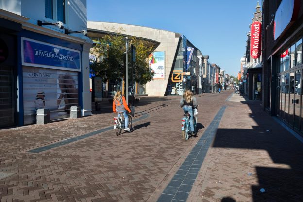 Twee meisjes fietsen door het een winkelstraat in het centrum van Apeldoorn.